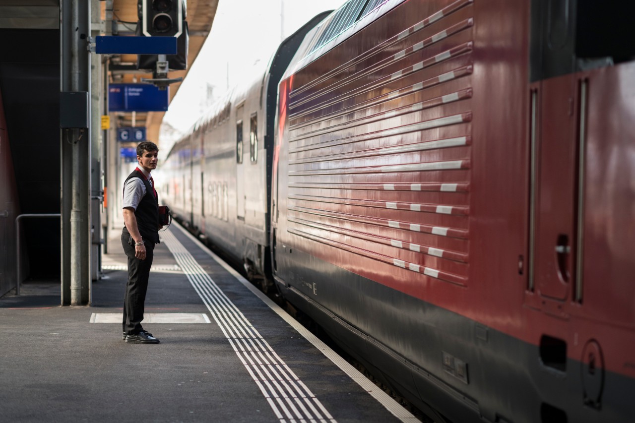 Ein SBB-Kundenbegleiter steht auf dem Perron neben einem Personenzug.